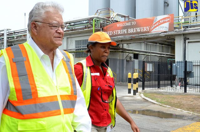 Industry, Commerce, Agriculture and Fisheries Minister, Hon. Karl Samuda (left) is being led on a tour of the Spanish Town Road-based Red Stripe plant by Local Raw Materials Business Development Manager, Dr. Cavell Francis-Rhiney discussing Cassava Farmers